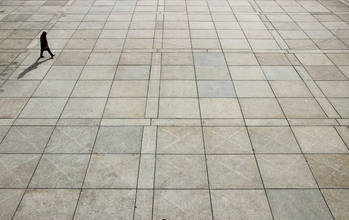 A man in an overcoat works across a floor with square tiles.